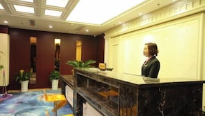A hotel reception area with a marble counter, potted plants, and a ceiling with skylights. - Jinlihua Hotel (Zhangjiagang)
