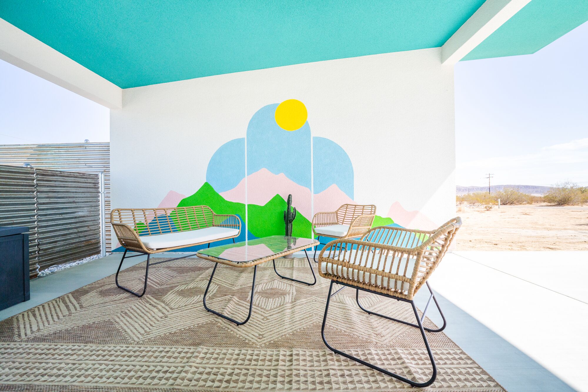 A room with two wicker chairs, a table, and a mural of mountains and a sun.