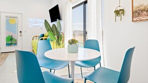 A modern room with a round table and blue chairs, a large window with a view, and a neon sign reading "California Dreaming". - New Listing Discount! Fire Pit~Hammocks (Joshua Tree)
