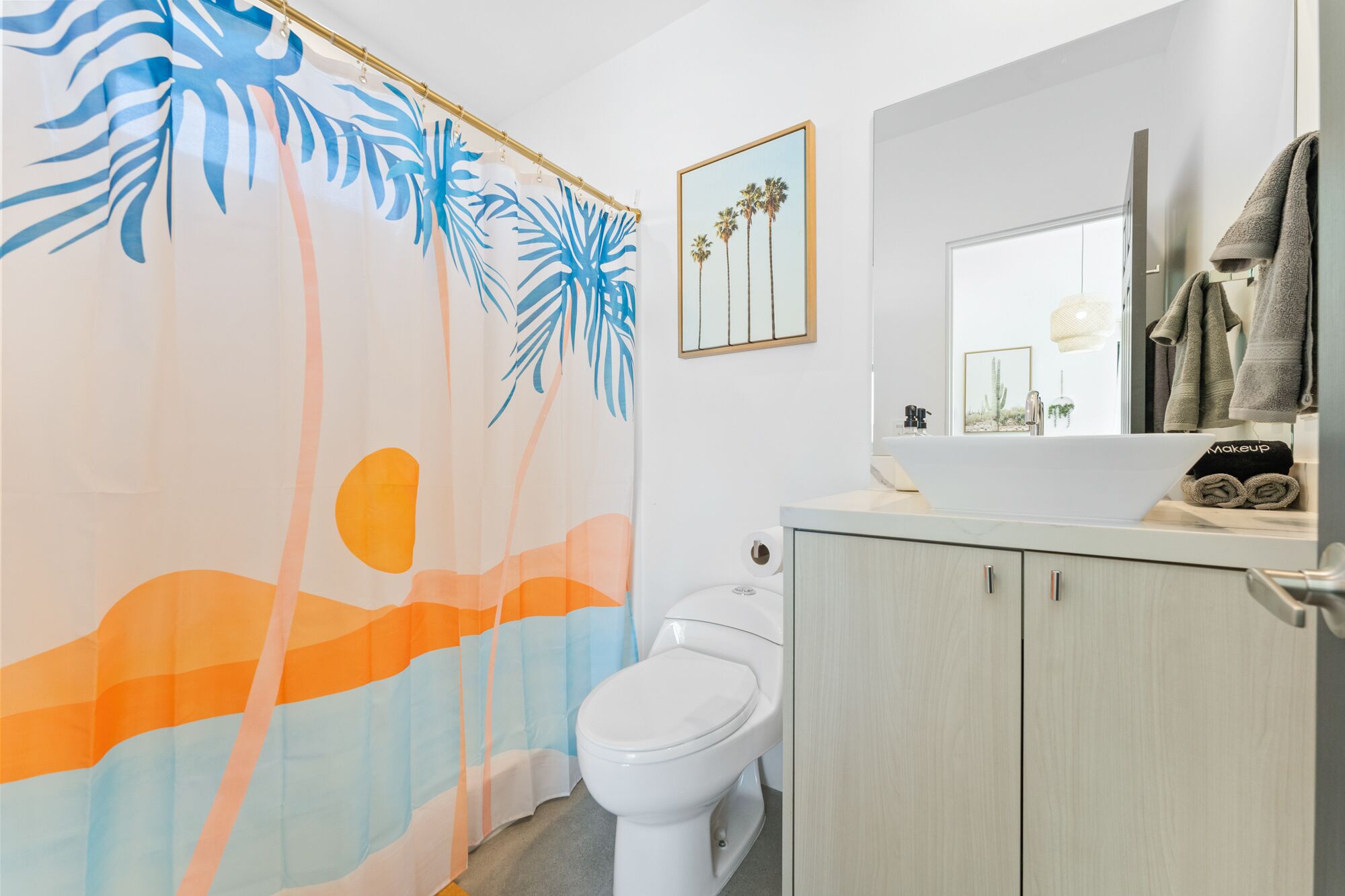 Une salle de bain équipée de toilettes, d’un lavabo et d’un rideau de douche orné de motifs de feuilles tropicales.