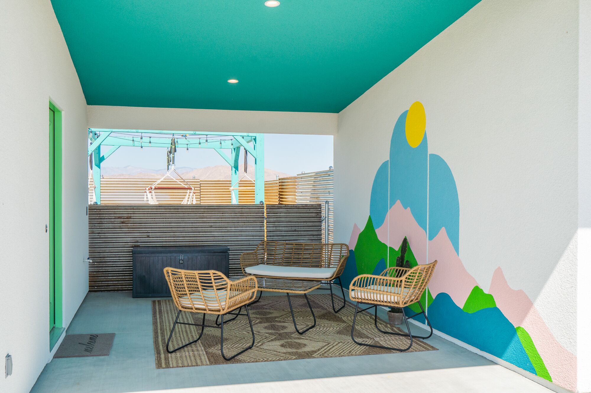 Una habitación con techo color turquesa, un mural de montañas y dos sillas de mimbre.
