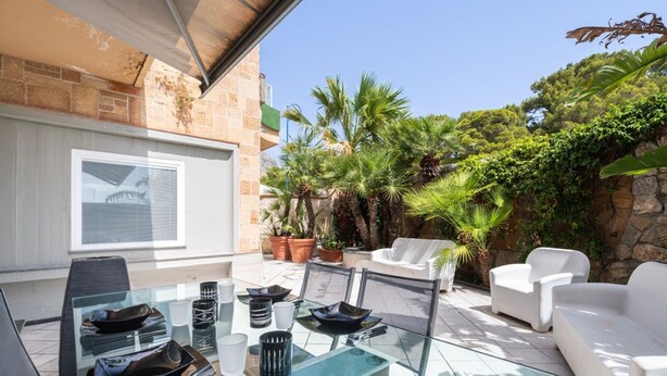 Eine Terrasse im Freien mit einem Glastisch, weißen Stühlen und Blumentöpfen.