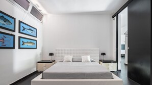 Ein modernes Schlafzimmer mit einem großen Bett, einem weißen Kopfschild, zwei Nachttischen und einem gerahmten Fischbild an der Wand.