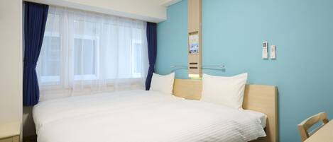 A hotel room with a large bed, a desk, and a chair. There is a window with curtains, a mirror, and a wall-mounted thermostat.