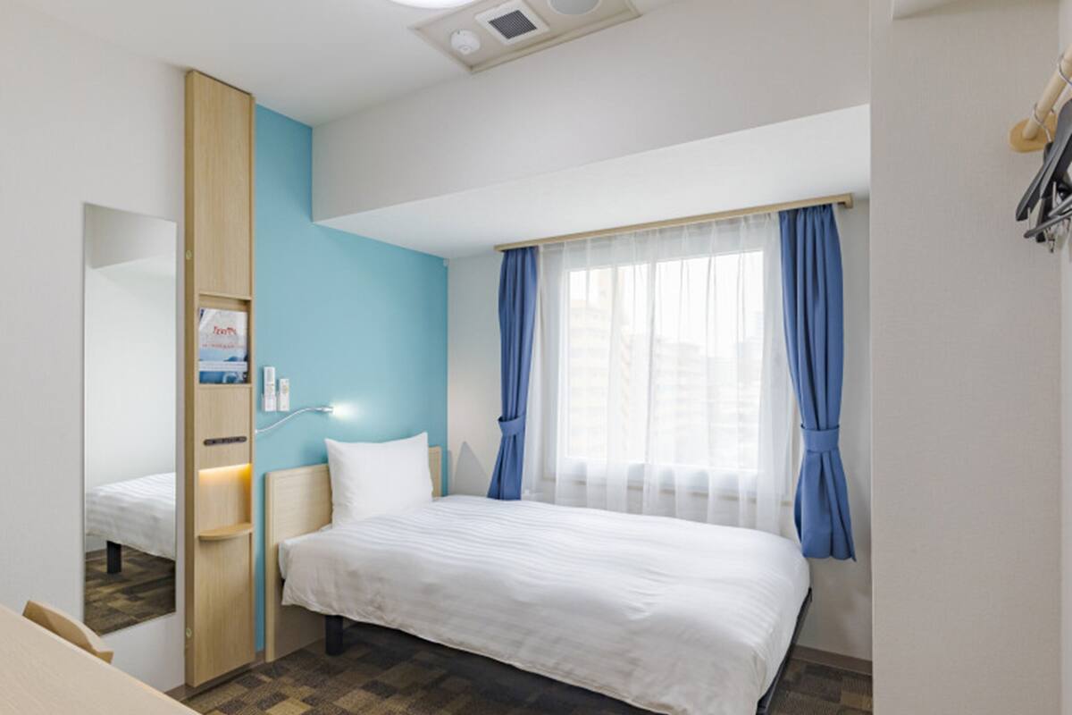 Une chambre d’hôtel comprenant un lit, un bureau, une armoire, une fenêtre avec des rideaux et un luminaire au plafond.