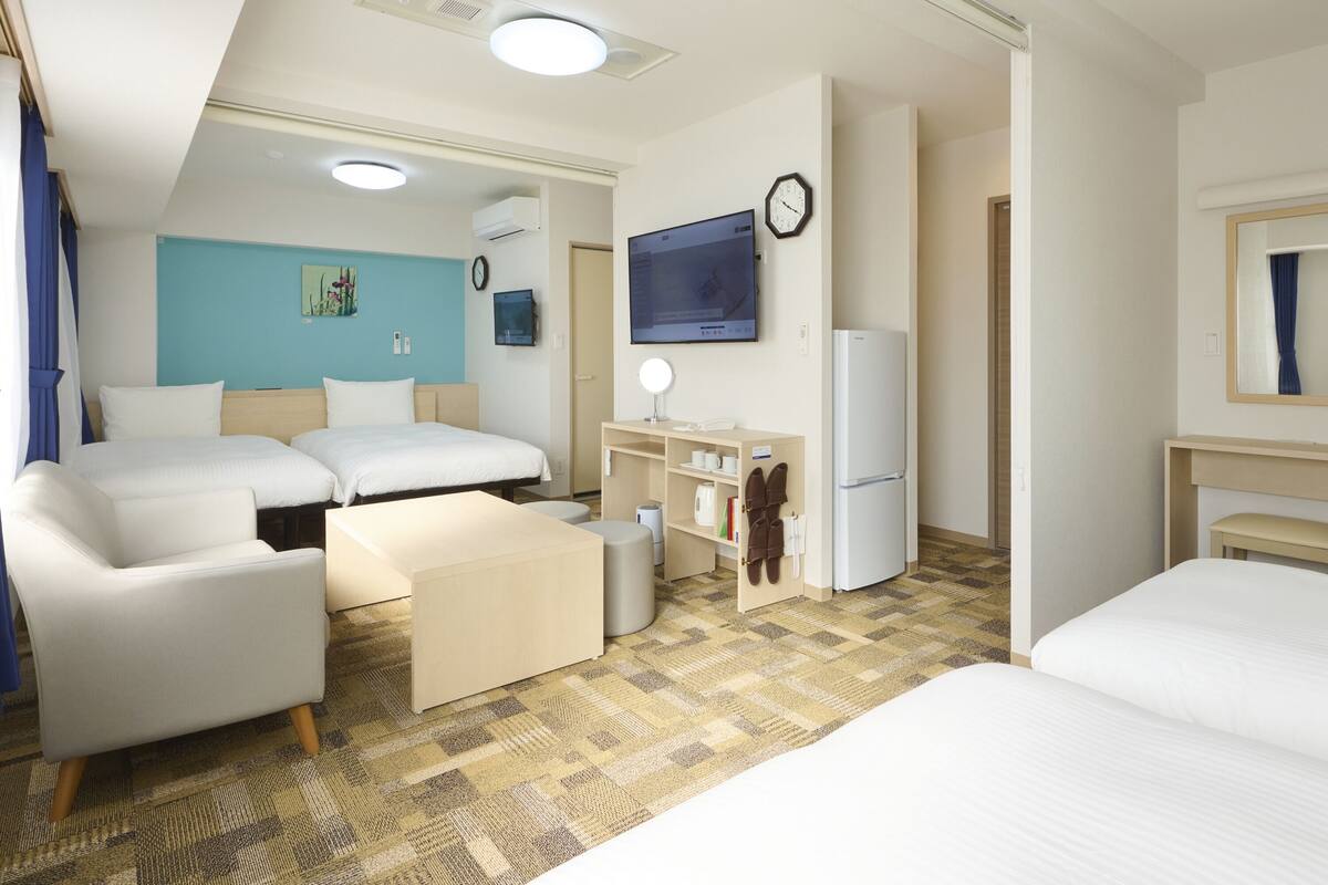 Une chambre d’hôtel avec deux lits, un canapé, une télévision, un réfrigérateur et un petit bureau avec un miroir.