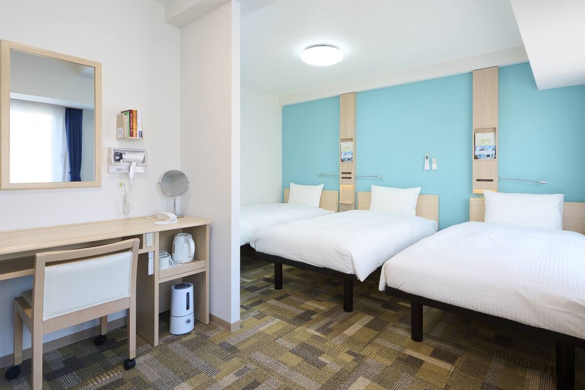 Une chambre d’hôtel avec deux lits, un bureau avec un miroir, un téléphone et une poubelle.
