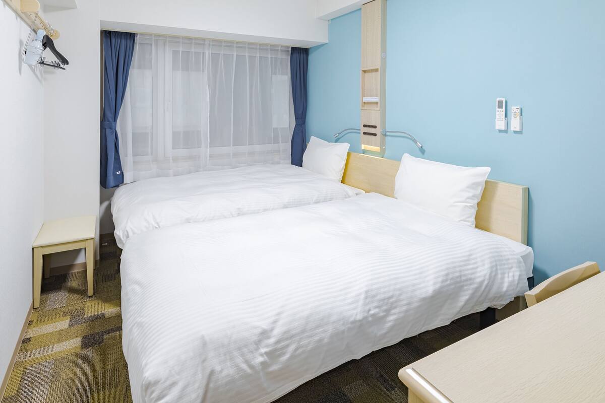 Une chambre d’hôtel avec deux lits, une petite table de chevet, une chaise, un miroir et un radiateur fixé au mur.