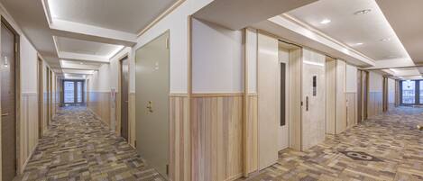Un largo pasillo de hotel, estrecho, con alfombra estampada, paneles de madera y puertas que dan a las habitaciones.