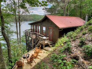 Uma cabana com varanda, área de estar externa e vista para um lago.
