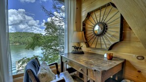 A wooden interior with a view of a lake, a wooden table with a lamp, and a chair. - The Blue Canoe | Cozy Lakefront Getaway in Blue Ridge | Rustic and Elegant  (Blue Ridge)