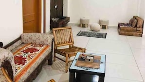 Un salon comprenant un canapé, deux fauteuils en bois, une table basse, un téléviseur et un ventilateur de plafond.