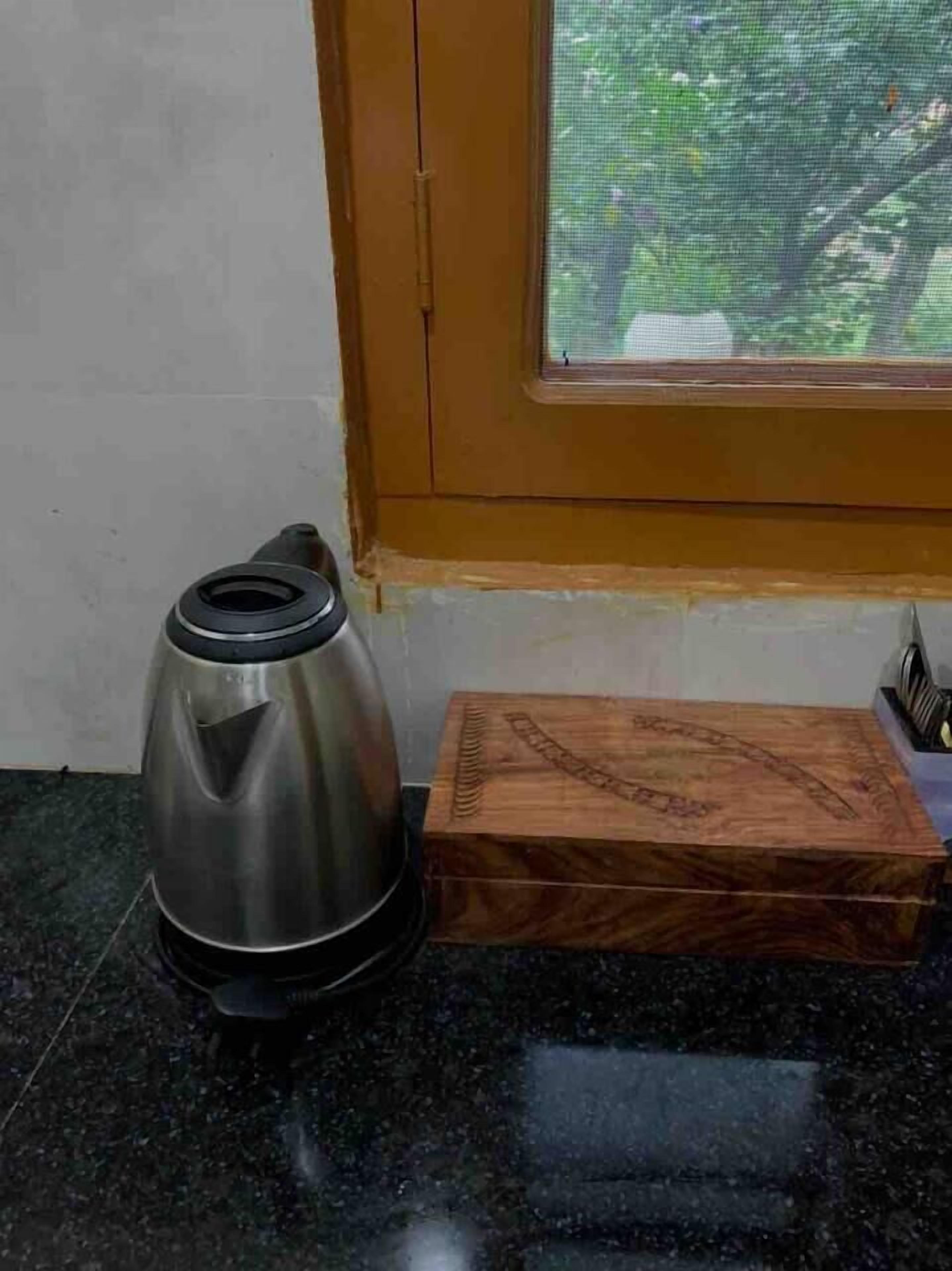 A stainless steel kettle on a black countertop next to a wooden box with a carved design.