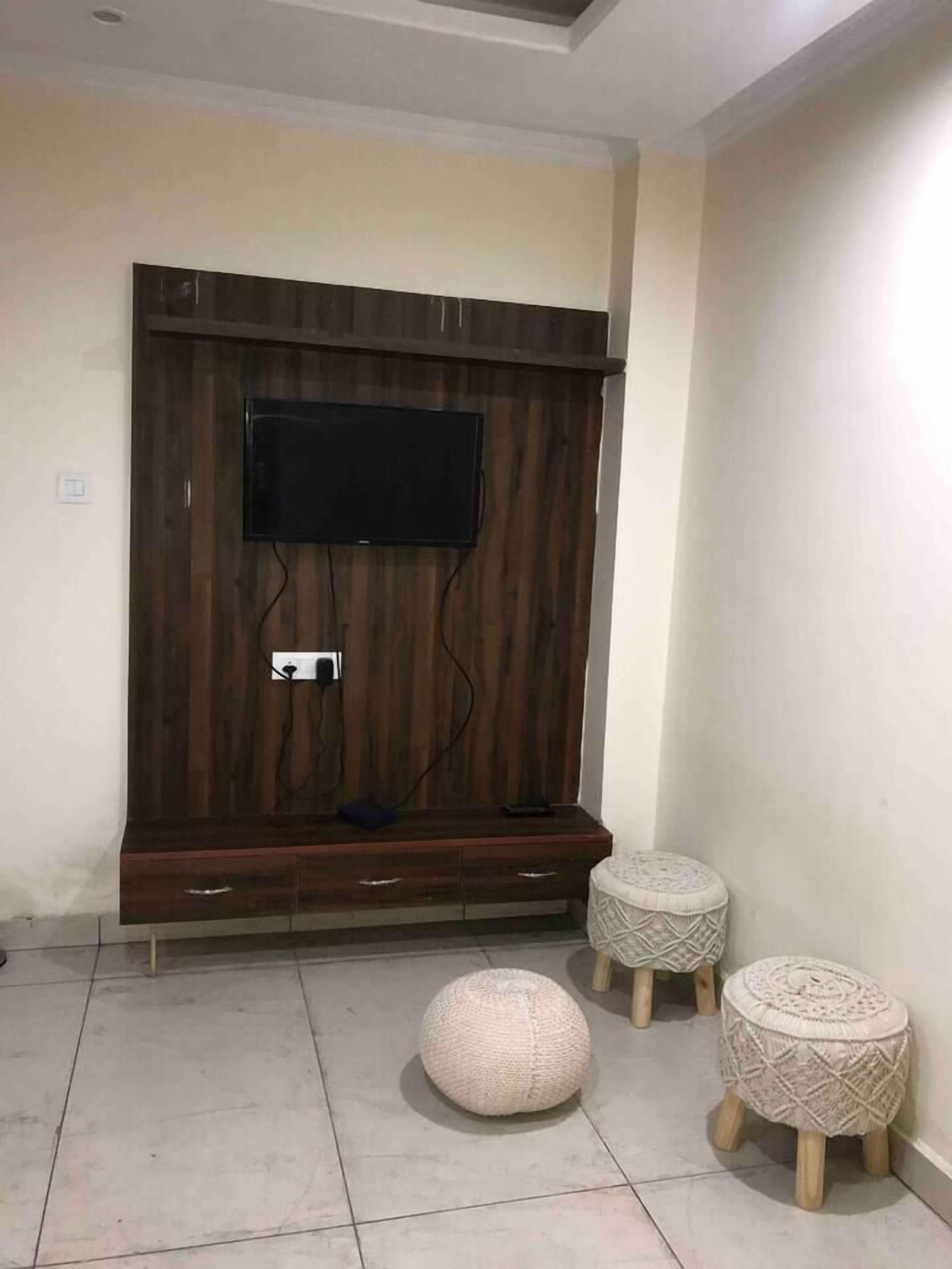 Une pièce dotée d’un meuble de rangement en bois pour les appareils multimédias, d’un téléviseur à écran plat, de deux poufs ronds et d’un sol carrelé.