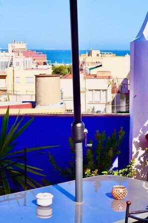 Un balcon offrant une vue dégagée sur la mer, un mur bleu et une table agrémentée d’un vase décoratif.