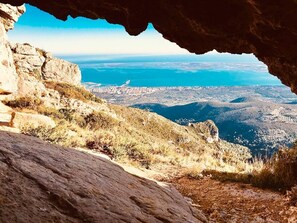 Un paysage rocheux offrant une vue sur une ville côtière, visible à travers l’ouverture d’une grotte.