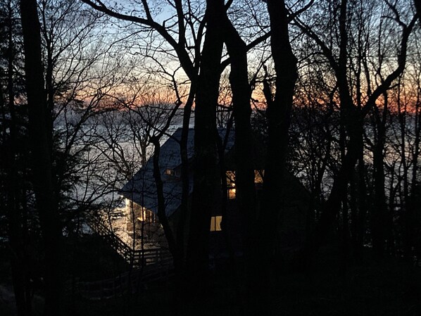 A house silhouetted against a sunset with a lake in the background.