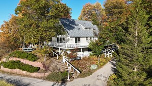 A house with a balcony, surrounded by trees and a stone pathway. - Sunset Serenity - INCREDIBLE HOME ON BLUFF OVERLOOKING LAKE MICHIGAN! (Frankfort)