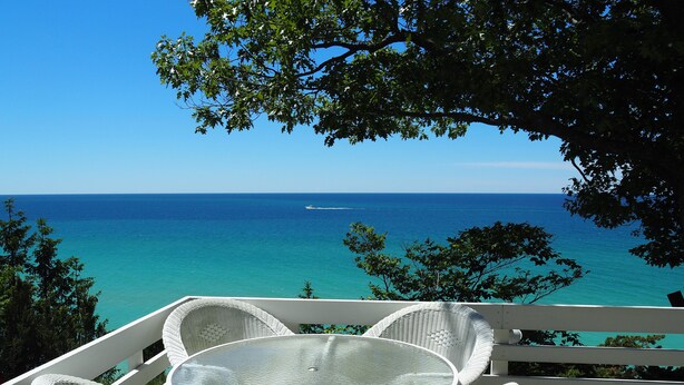 A balcony with wicker furniture overlooking a clear blue sea. - Sunset Serenity - INCREDIBLE HOME ON BLUFF OVERLOOKING LAKE MICHIGAN! (Frankfort)