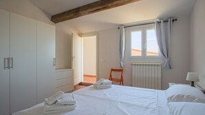 A bedroom with a bed, white wardrobe, wooden beams, a window with curtains, and a chair. - Benvenuto - Sweet Dreams in Florence (Firenze)