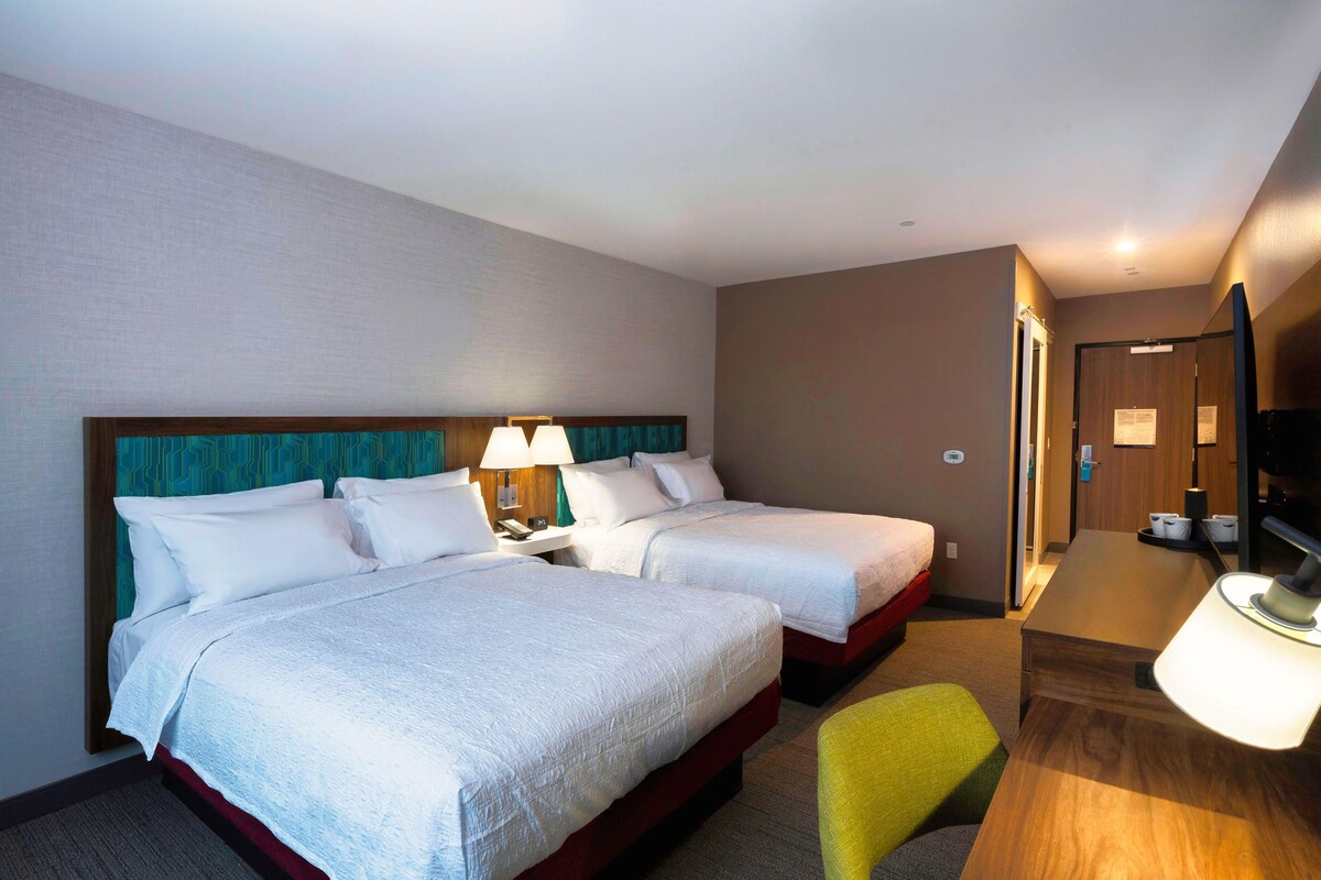 Una habitación de hotel con dos camas, un escritorio, una silla y un televisor.