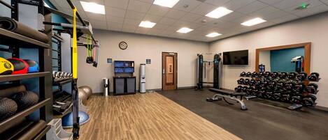 A gym with exercise equipment, a clock, a TV, and a mirror.