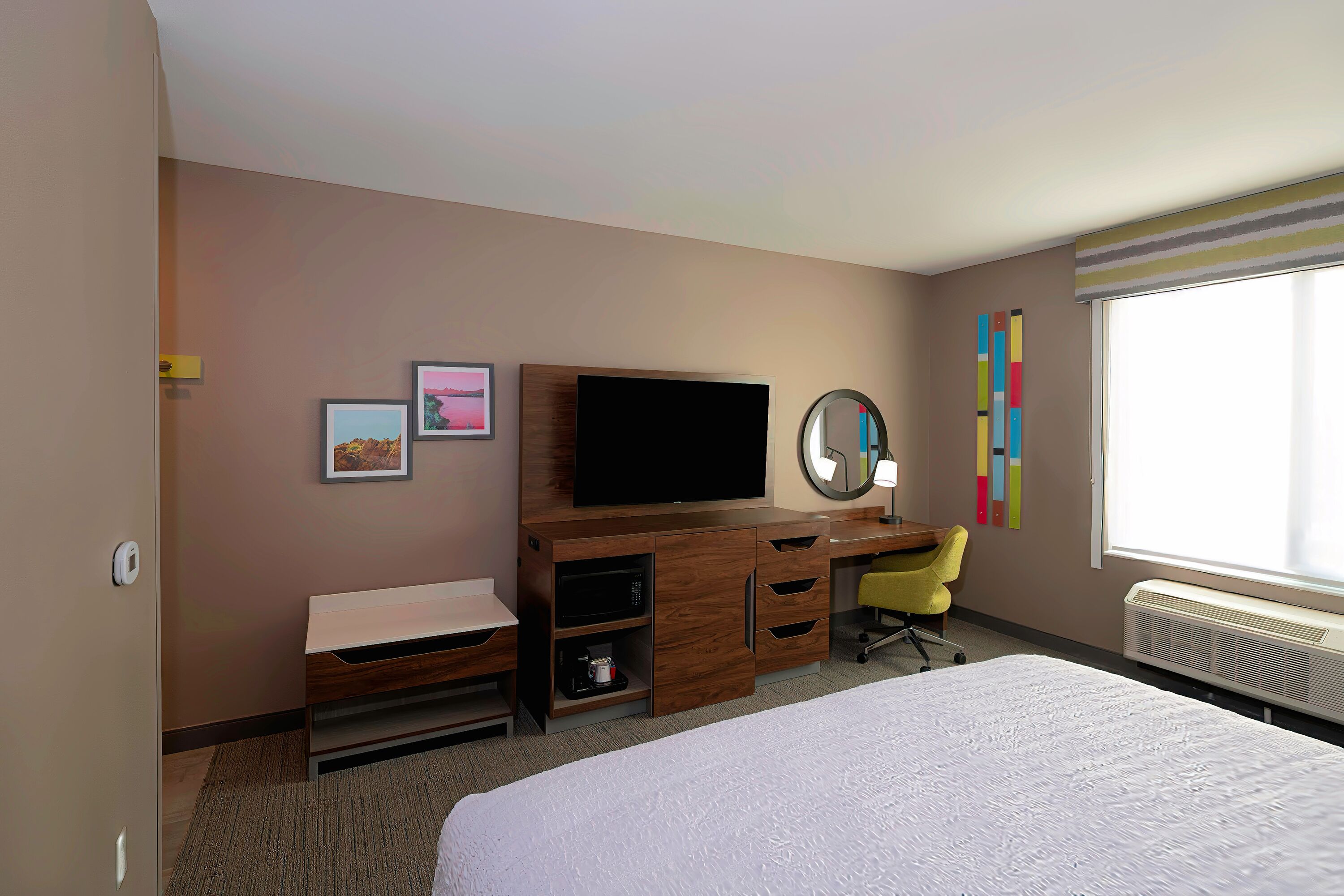 Habitación de hotel con cama, escritorio, televisor, espejo y ventana con persianas.