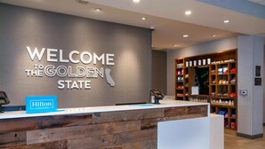 Una mesa de recepción con un letrero que dice 'Welcome to the Golden State', una insignia de 'Hilton Honors' y una zona de exhibición de libros.