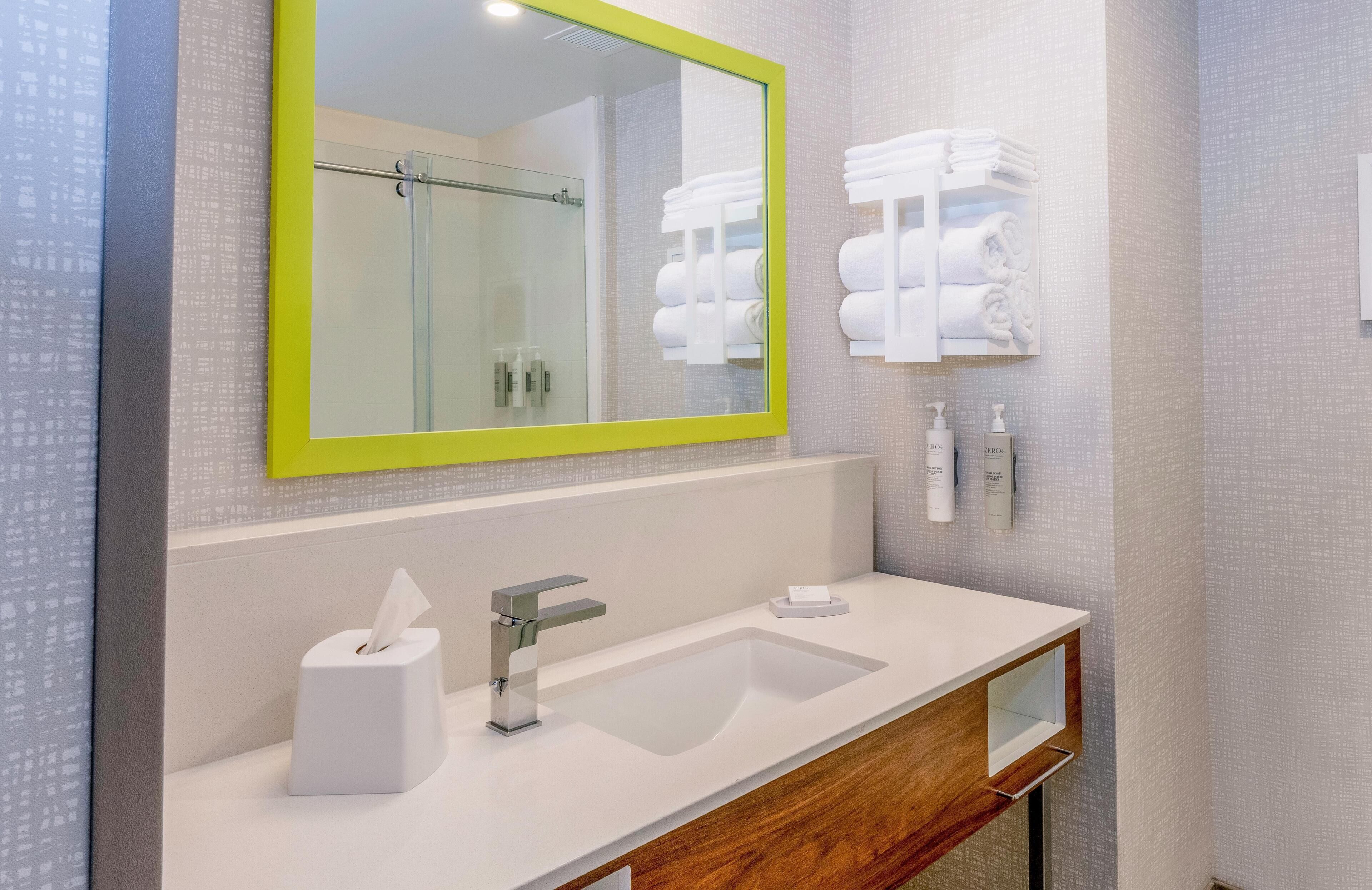 A modern bathroom with a large mirror, a sink, a towel rack, and a shower area.