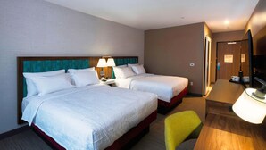 Habitación de hotel con dos camas, un escritorio y una televisión.
