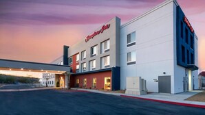 Un hotel Hampton Inn con fachada moderna, múltiples ventanas y cielo despejado.