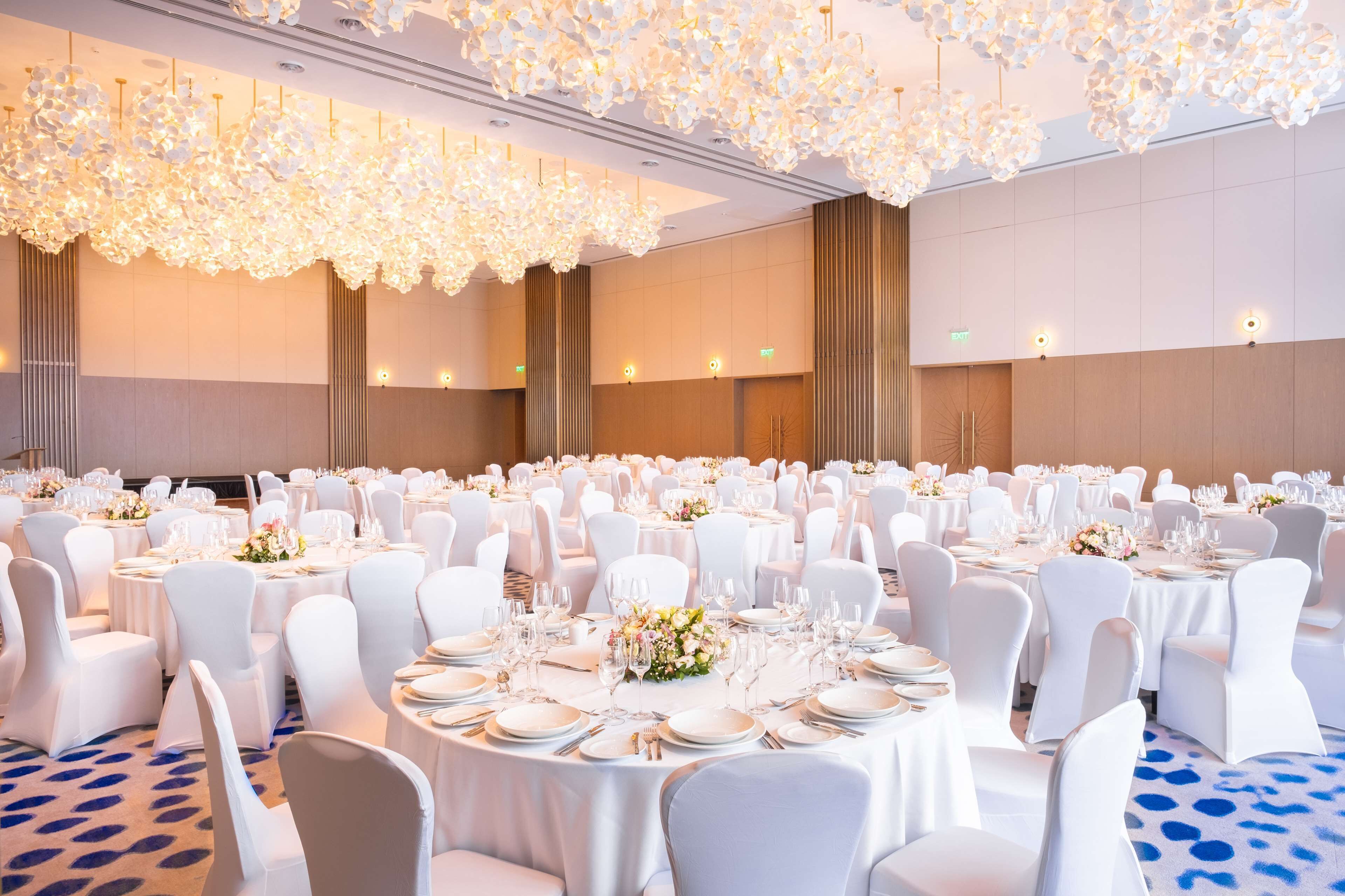 A banquet hall with round tables set for dining, white chairs, and chandeliers.