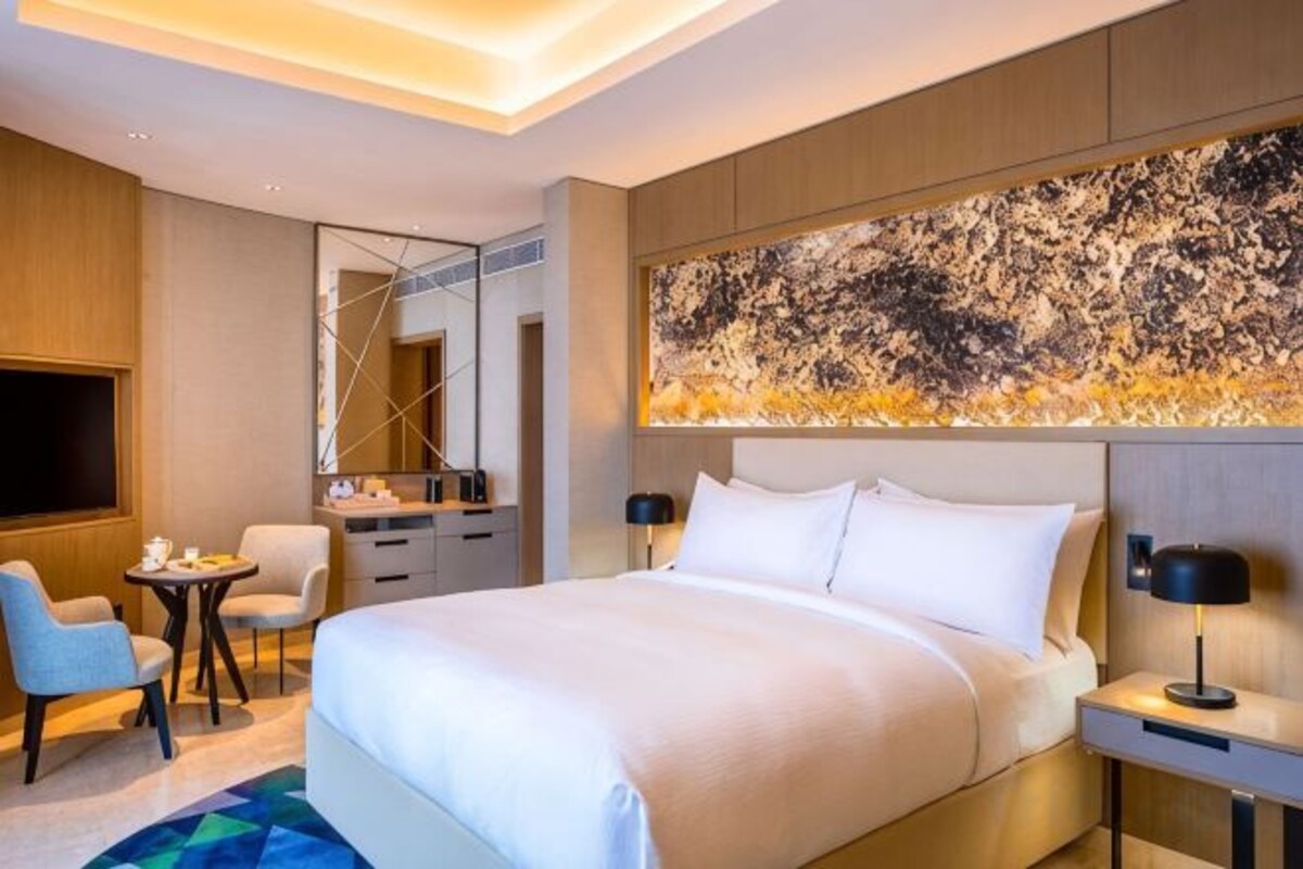 Habitación de hotel moderna con una cama grande, un escritorio, una silla, un televisor y un cuadro abstracto de grandes dimensiones en la pared.