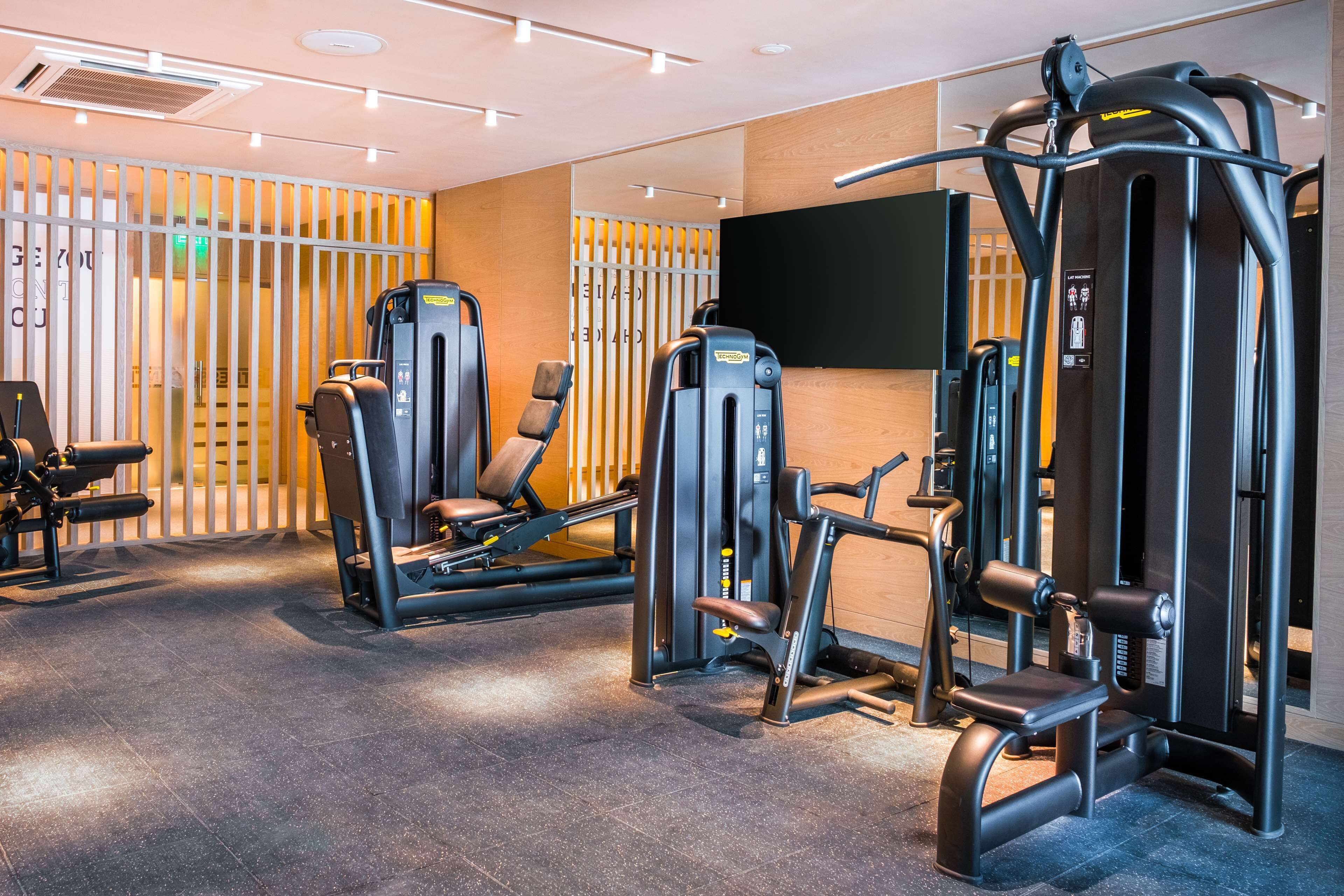 A gym with various exercise machines, a large screen, and a wooden wall with a vertical divider.