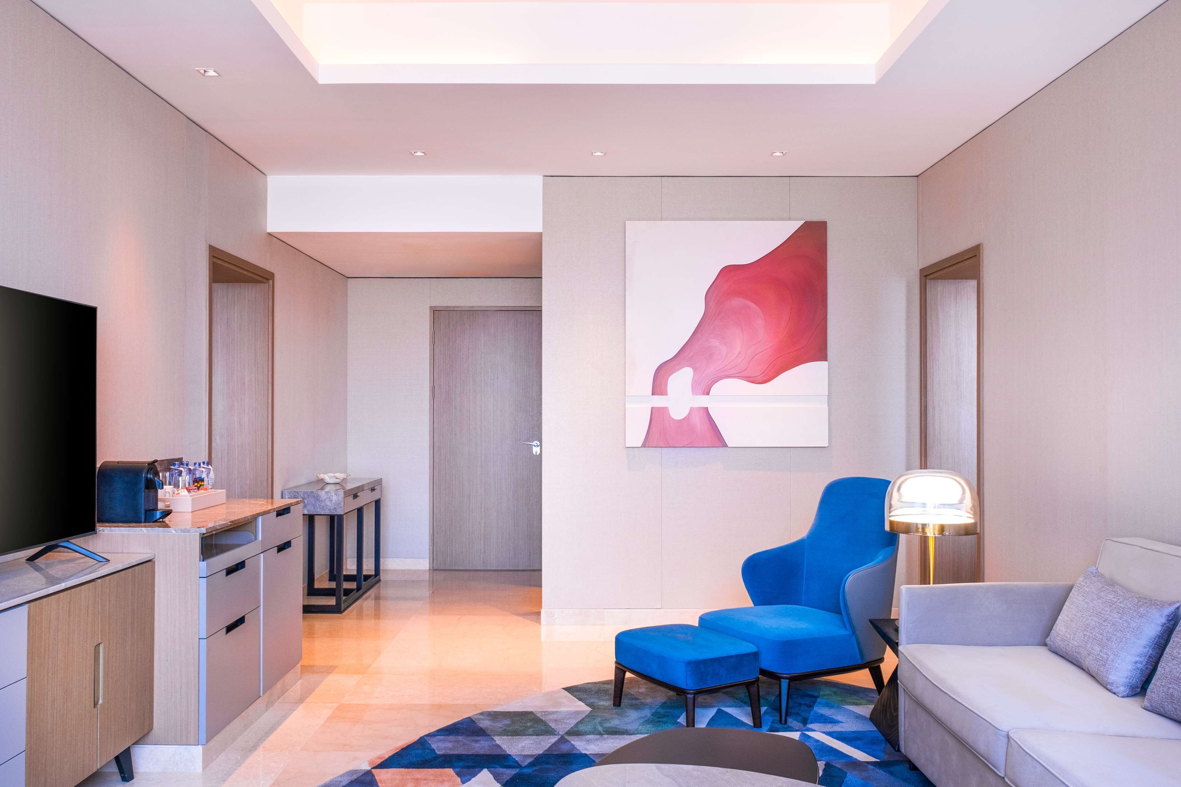 A modern living room with a flat-screen TV, a sofa, a blue armchair, a coffee table, and a painting on the wall.