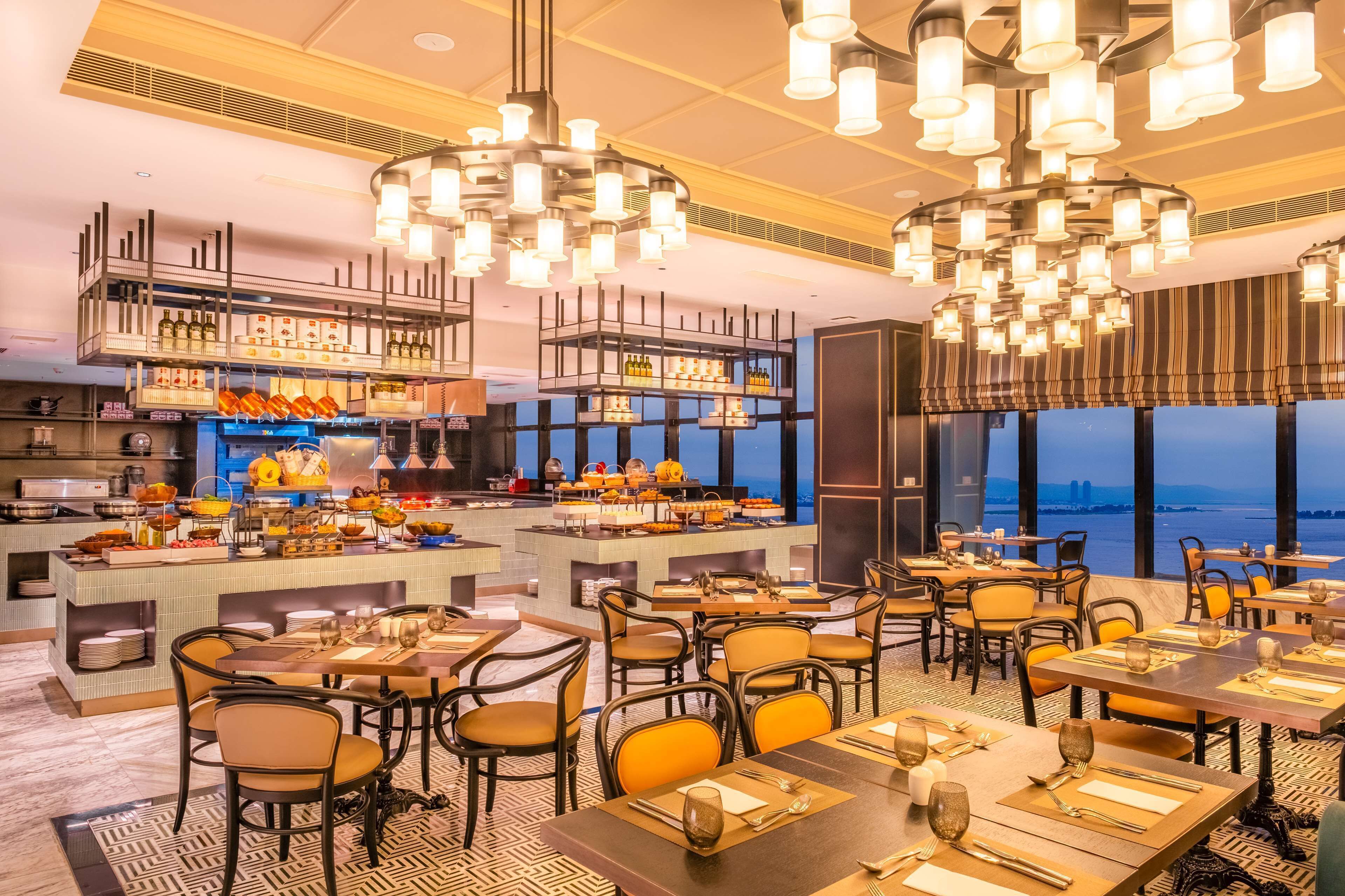 Un restaurant doté de nombreuses tables et chaises, d’un bar avec des bouteilles exposées, et offrant une vue sur le paysage urbain.