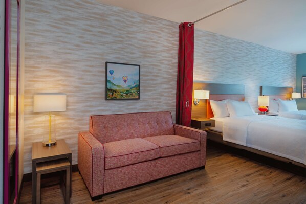A hotel room with a red sofa, a bed, a nightstand with a lamp, and a wall with a textured pattern.
