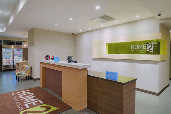 A hotel reception desk with a 'HOME 2' sign, a seating area with a colorful chair, and a reception counter.