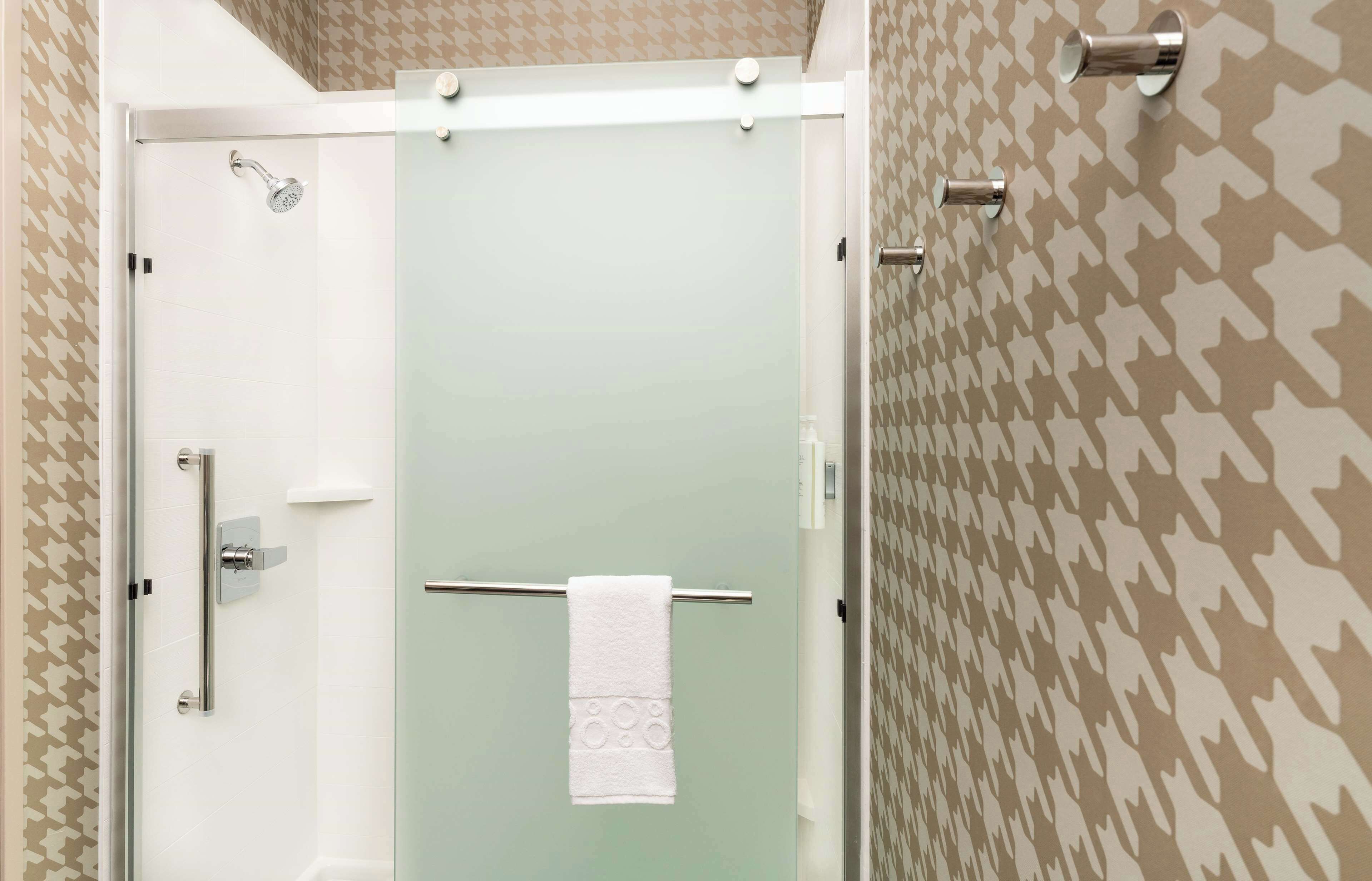 Un baño con mampara de vidrio, una toalla colgada en un perchero y papel tapiz estampado.