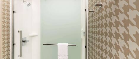 Un baño con mampara de vidrio, una toalla colgada en un perchero y papel tapiz estampado.