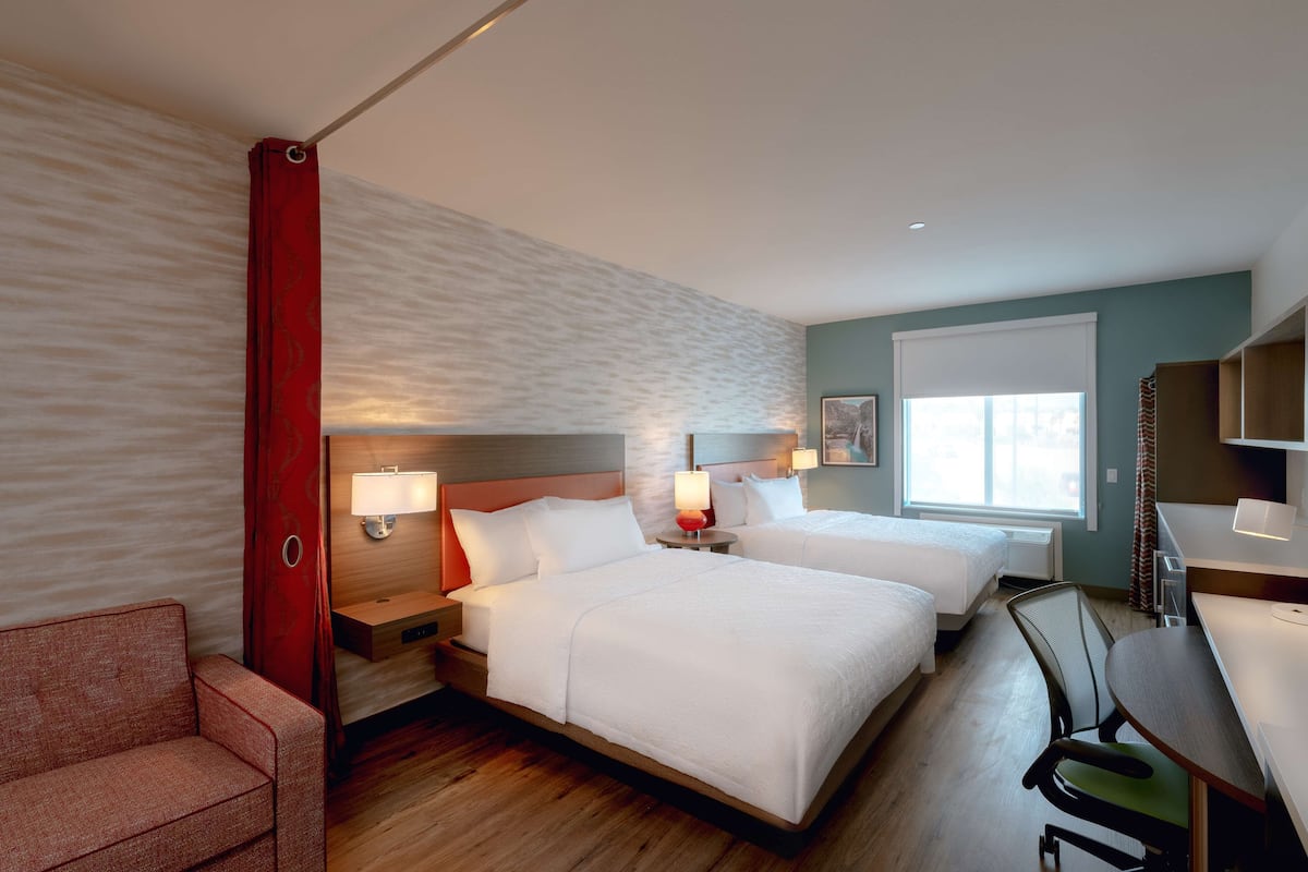 Quarto de hotel com duas camas, uma mesa, uma cadeira e um sofá.