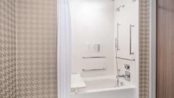 A modern bathroom with a bathtub, shower, and handrails.
