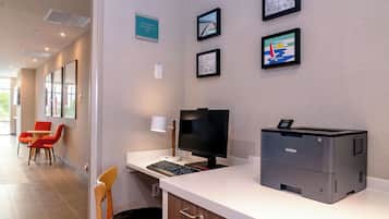 A reception desk with a Brother printer, framed artwork on the wall, and a seating area with orange chairs.