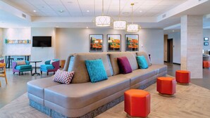 A modern lobby with a curved sofa, colorful cushions, orange ottomans, and a flat-screen TV on the wall. - Home2 Suites Lake Havasu City, Az (Lake Havasu City)