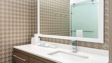 A bathroom with a houndstooth patterned wallpaper, a white sink, a mirror, and wooden cabinetry.
