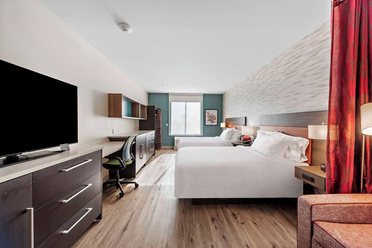 Een moderne hotelkamer met een grote flatscreen-tv, een bureau met stoel, een bed met twee kussens en een nachtkastje met lamp.