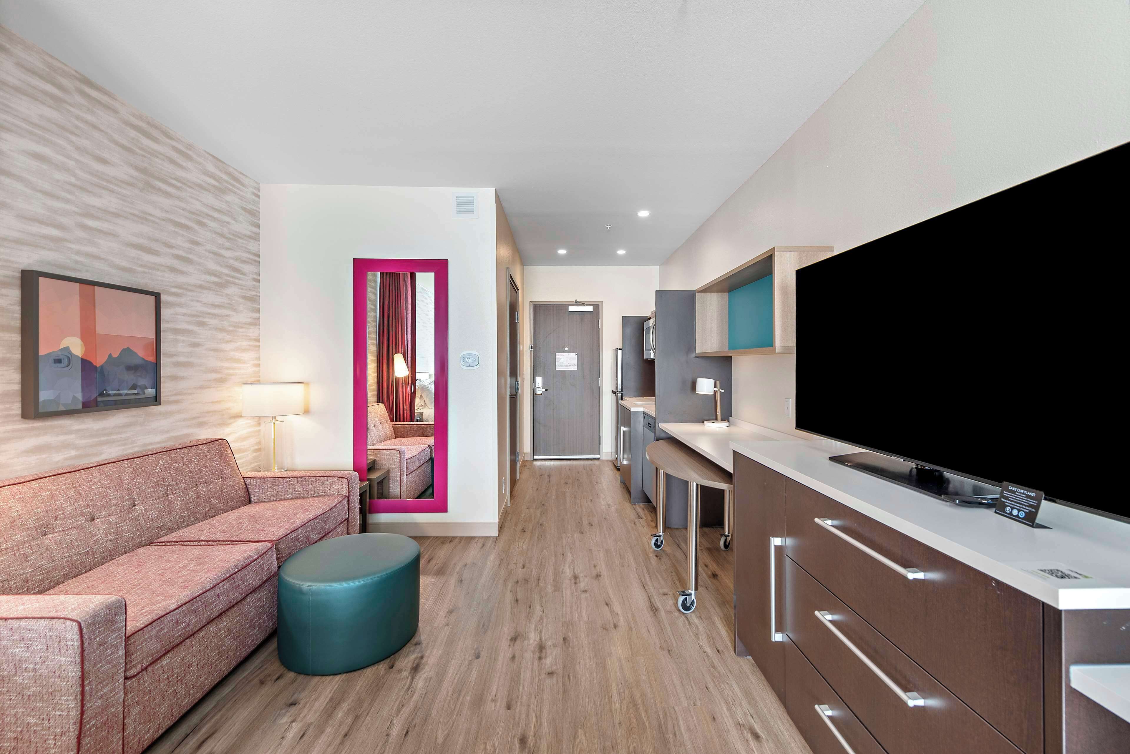 Una habitación de hotel moderna con sofá, reposapiés y un televisor de pantalla plana grande.