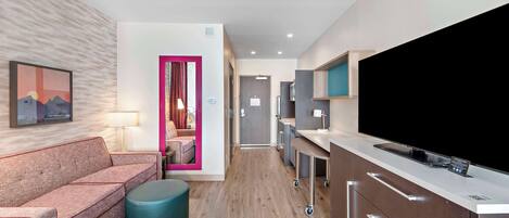 Una habitación de hotel moderna con sofá, reposapiés y un televisor de pantalla plana grande.