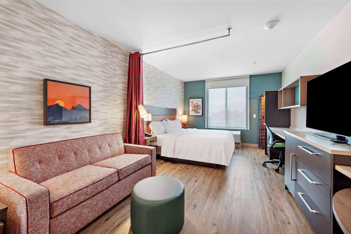 Een moderne hotelkamer met een bed, een slaapbank, een bureau en een televisie.
