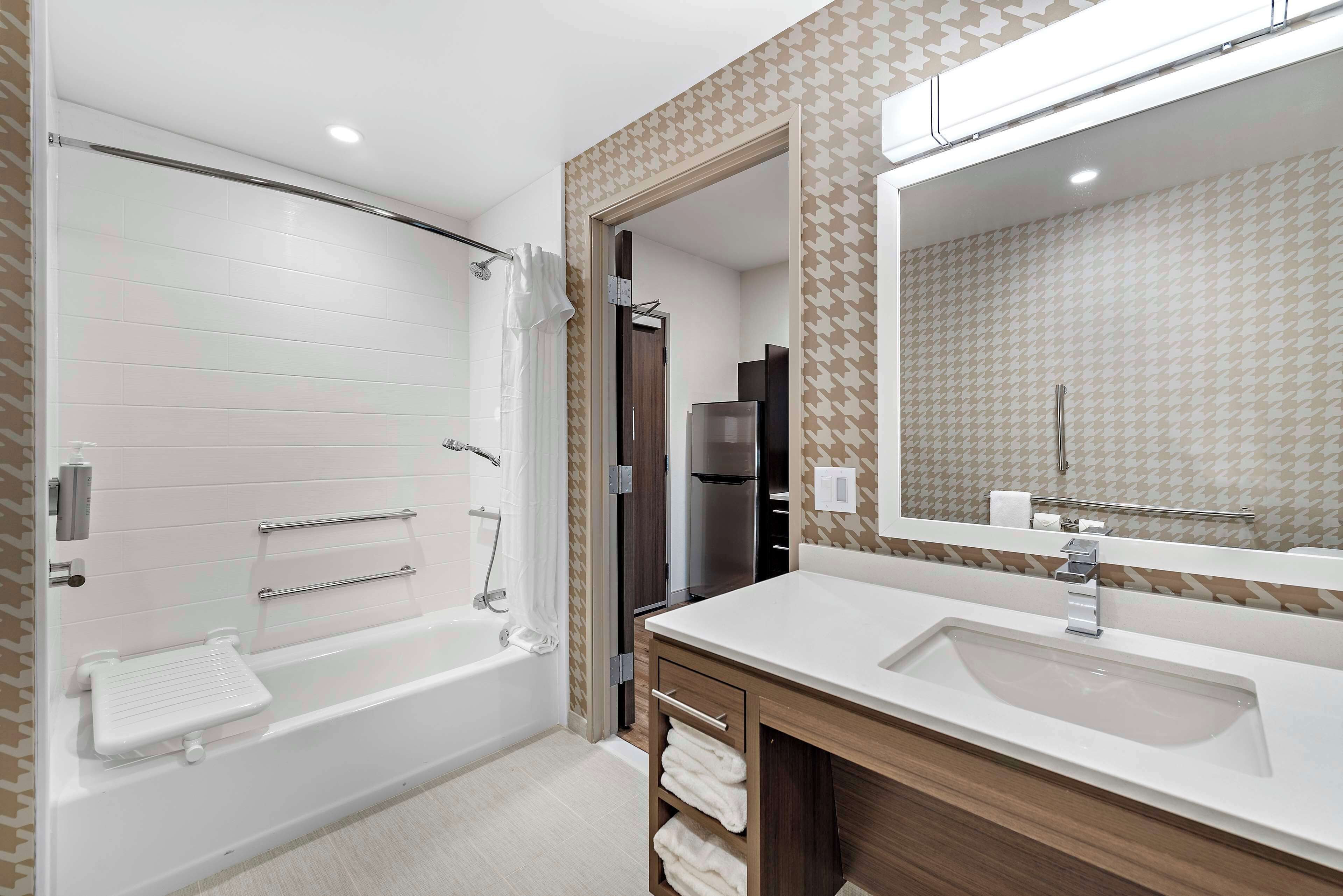 A modern bathroom with a bathtub, a large mirror, and a vanity with a sink.
